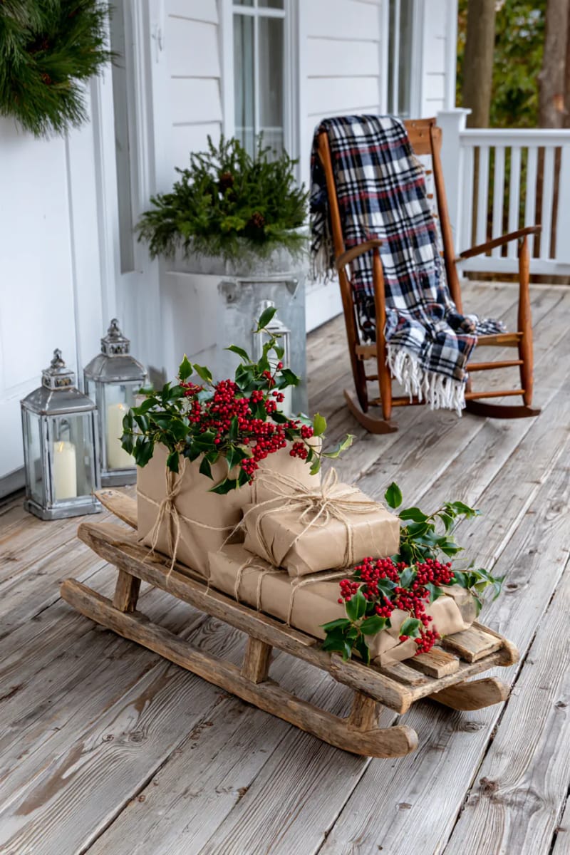 15 Cozy Rustic Christmas Porch Ideas for Country Charm 12 wooden sled propped beside the door with jute-wrapped gifts and holly sprigs 1
