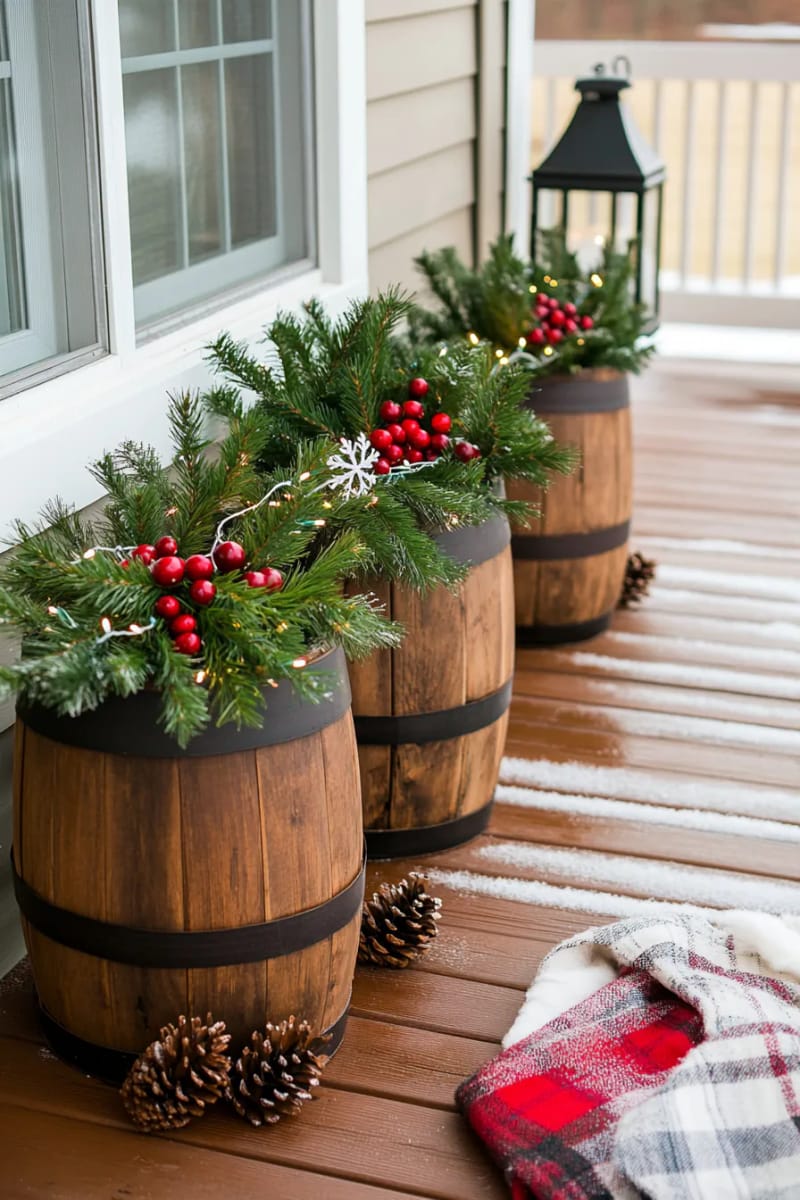 barrel planters filled with evergreen branches, cranberries, and white fairy lights 1