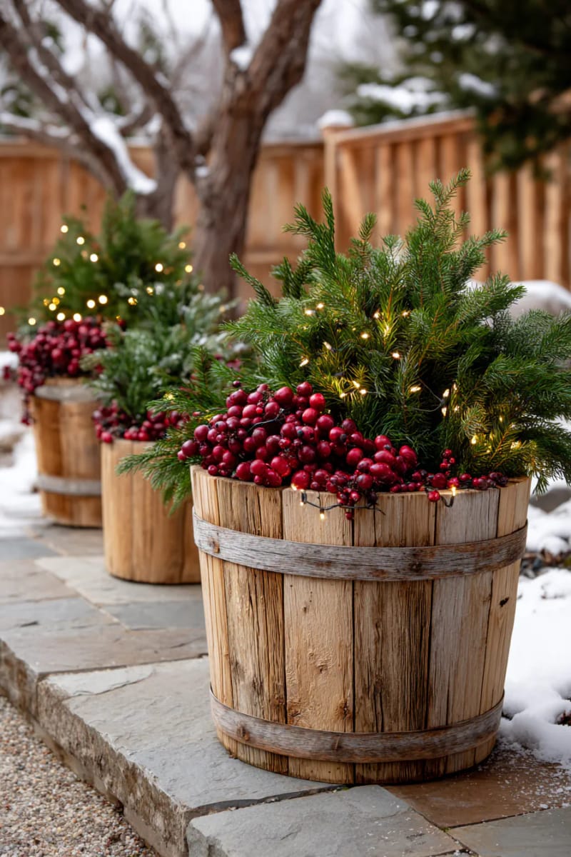 barrel planters filled with evergreen branches, cranberries, and white fairy lights 1