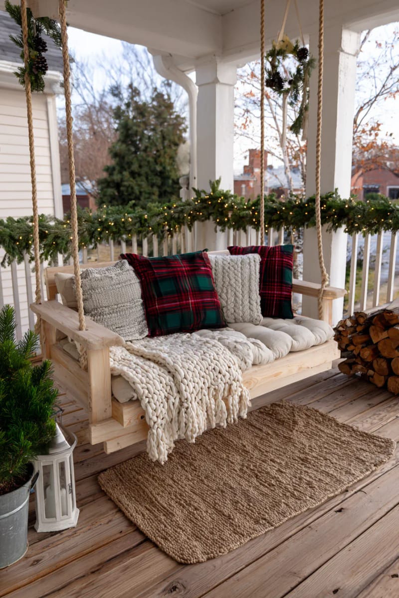 15 Simple Farmhouse Christmas Front Porch Decor Ideas 21 cozy plaid pillows and chunky throws on porch swing for a winter nook 1