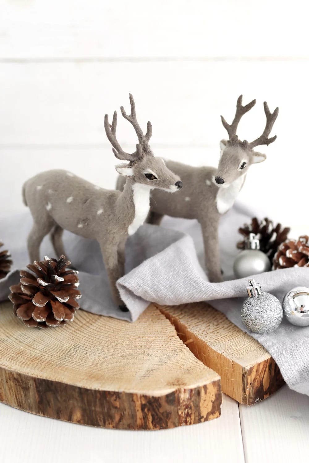 Wood Slice Christmas Ornaments With Wood Burned Designs That Don't Look Like a Kit 12 Two decorative deer figurines on a wood slice with pine cones and silver ornaments, illustrating a setup for wood slice Christmas ornaments with a wood burned deer silhouette theme.