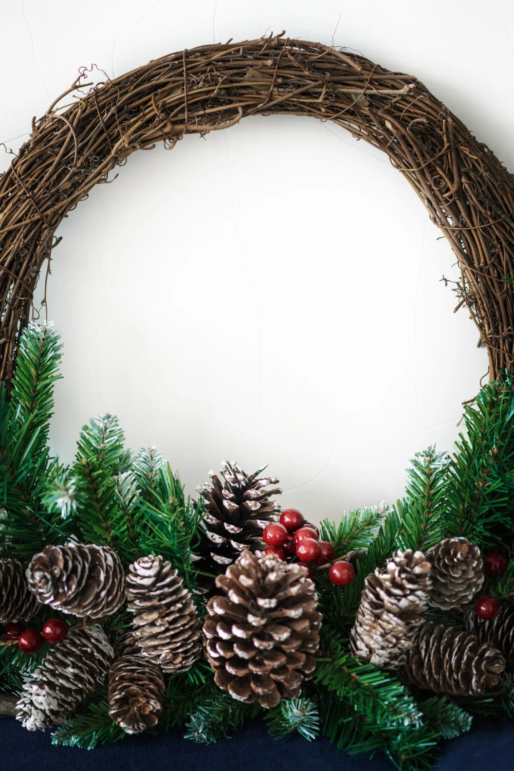 Foraged Twig Christmas Decorations From the Garden 2 A handmade Christmas wreath crafted from foraged willow twigs, decorated at the bottom with pinecones, artificial evergreen branches, and red berries, illustrating a natural alternative to a foam base for garden-inspired holiday decorations.