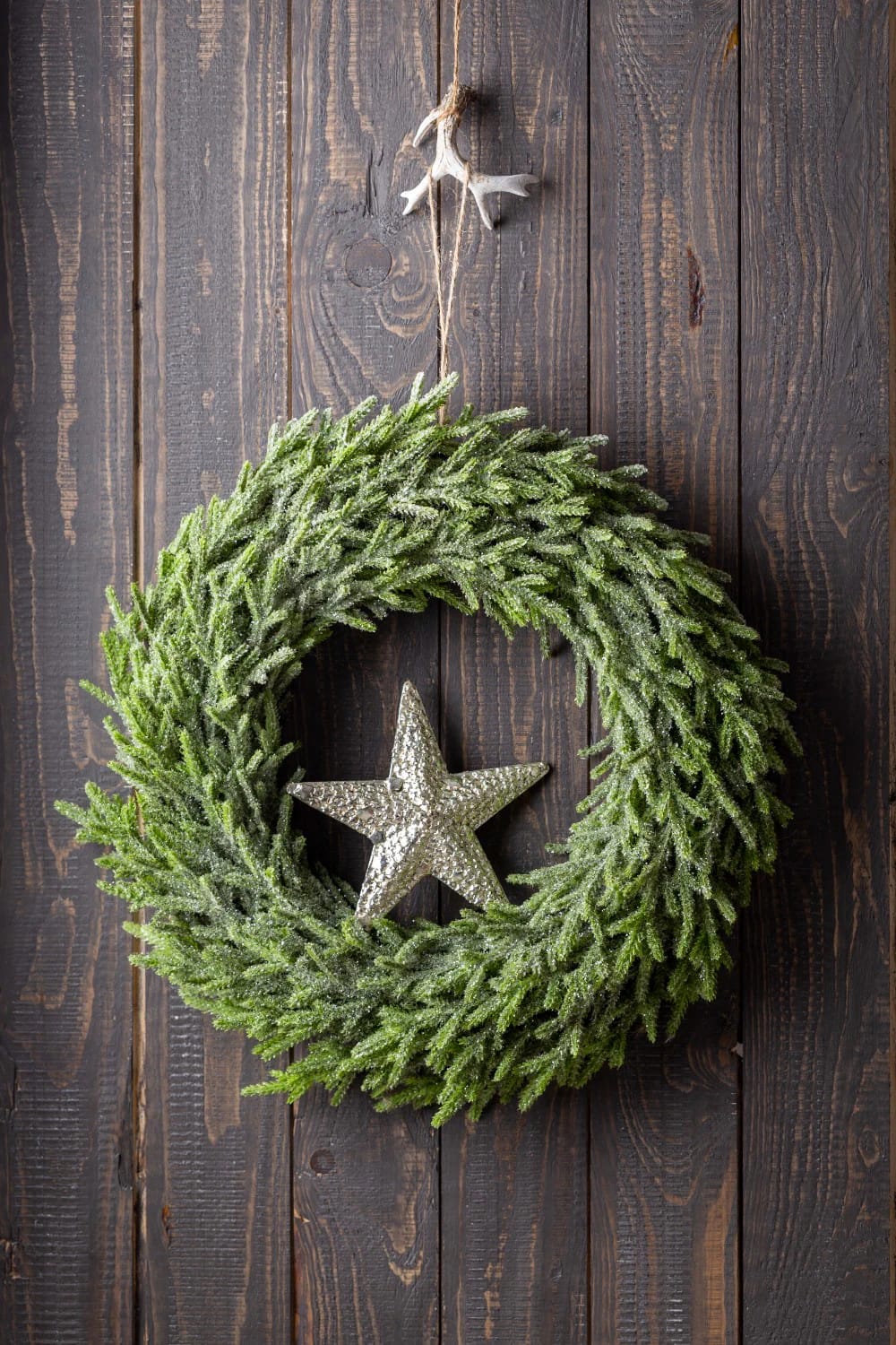 Foraged Twig Christmas Decorations From the Garden 4 A handmade Christmas wreath made from foraged willow twigs, decorated with a sparkling silver star and hanging on a rustic wooden wall, illustrating a natural alternative to foam bases for festive garden decorations.