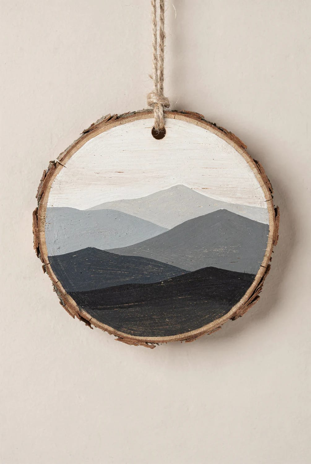 13 Painted Wood Slice Ornaments for a Minimalist Tree 7 A painted wood slice ornament featuring a layered mountain range in neutral gray tones, designed for a minimalist tree, with a rustic twine loop for hanging.