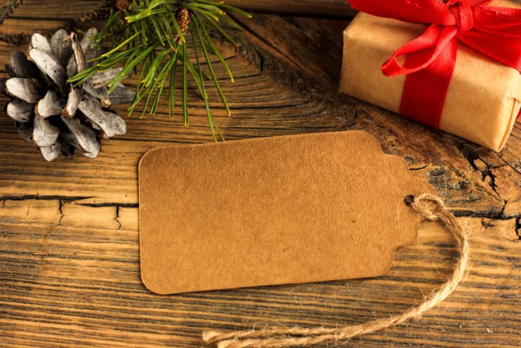 Sustainability Success 9 A brown paper card with twine lies on rustic wood beside a wrapped gift with a red ribbon and a pinecone, illustrating a brown paper and twine Christmas place card setup.