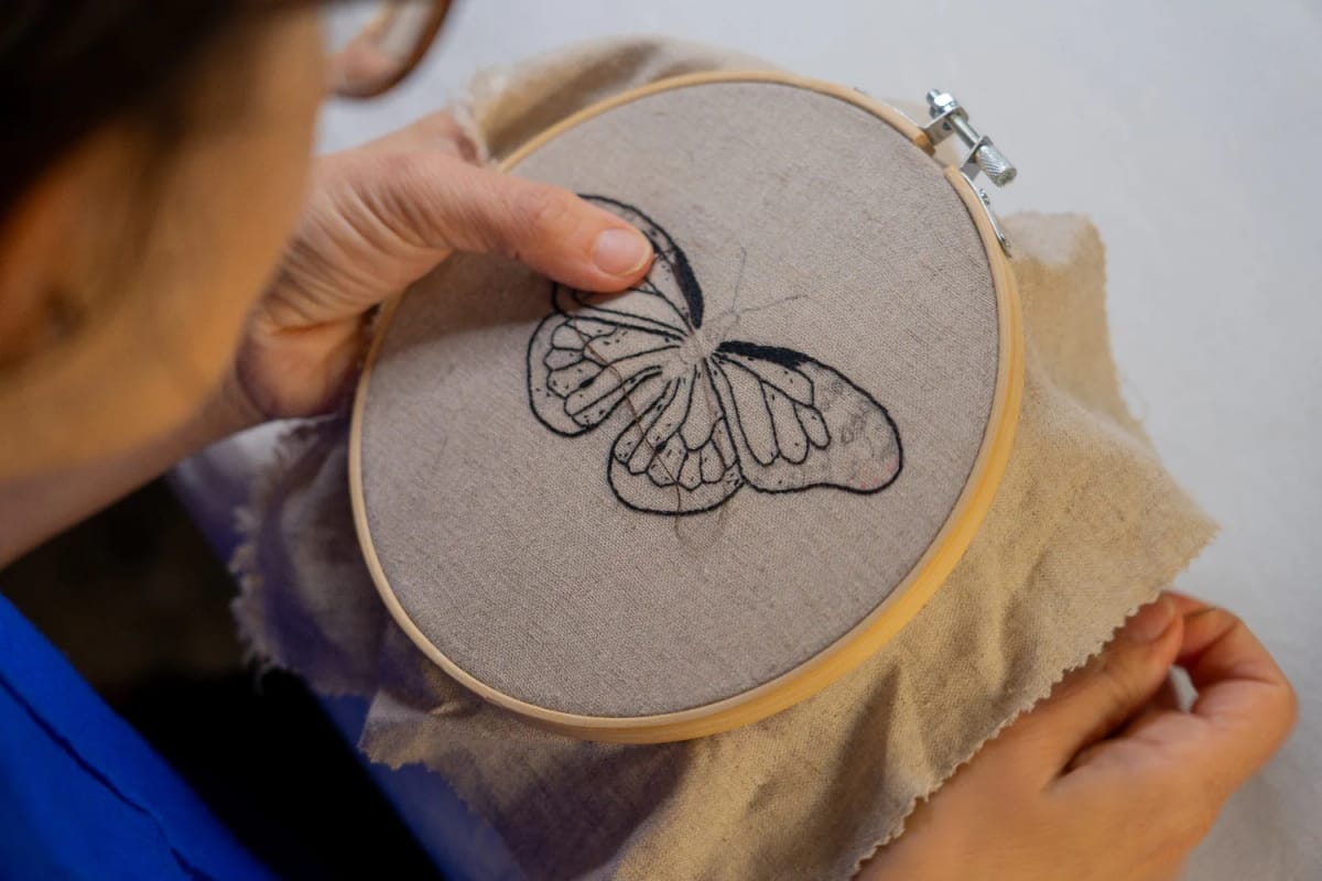 Butterfly Embroidery Jeans Design Close-up of hands holding an embroidery hoop with a butterfly design outlined on fabric, illustrating a butterfly embroidery idea for jeans