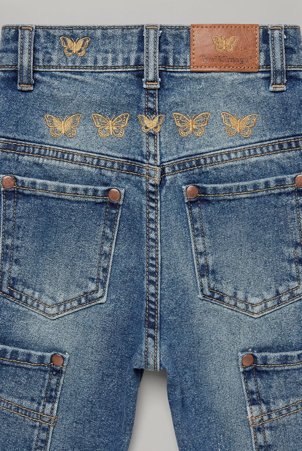 Butterfly Embroidery Jeans With Gold Thread Close-up of blue denim jeans featuring five gold butterfly embroidery designs across the back yoke, one butterfly above the left pocket, matching gold topstitching, brown rivets, rear pockets, belt loops, and a leather waistband label
