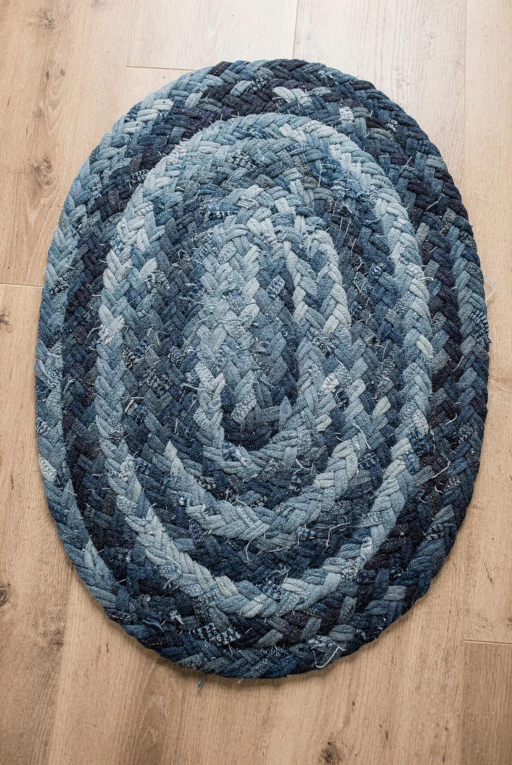 How to Make a Braided Denim Rag Rug From Old Jeans 3 Oval braided denim rag rug made from old jeans, with blue fabric strips coiled and laced together on a wooden floor