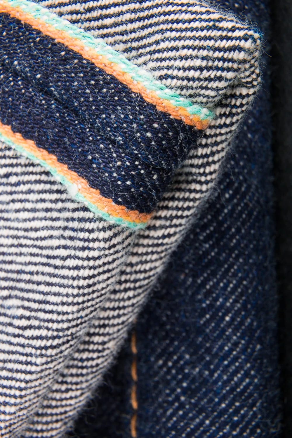 Colorful Thread Darning On Jeans Close-up of dark denim jeans with a sashiko-style striped knee panel and bright orange and mint-green stitching along its edges