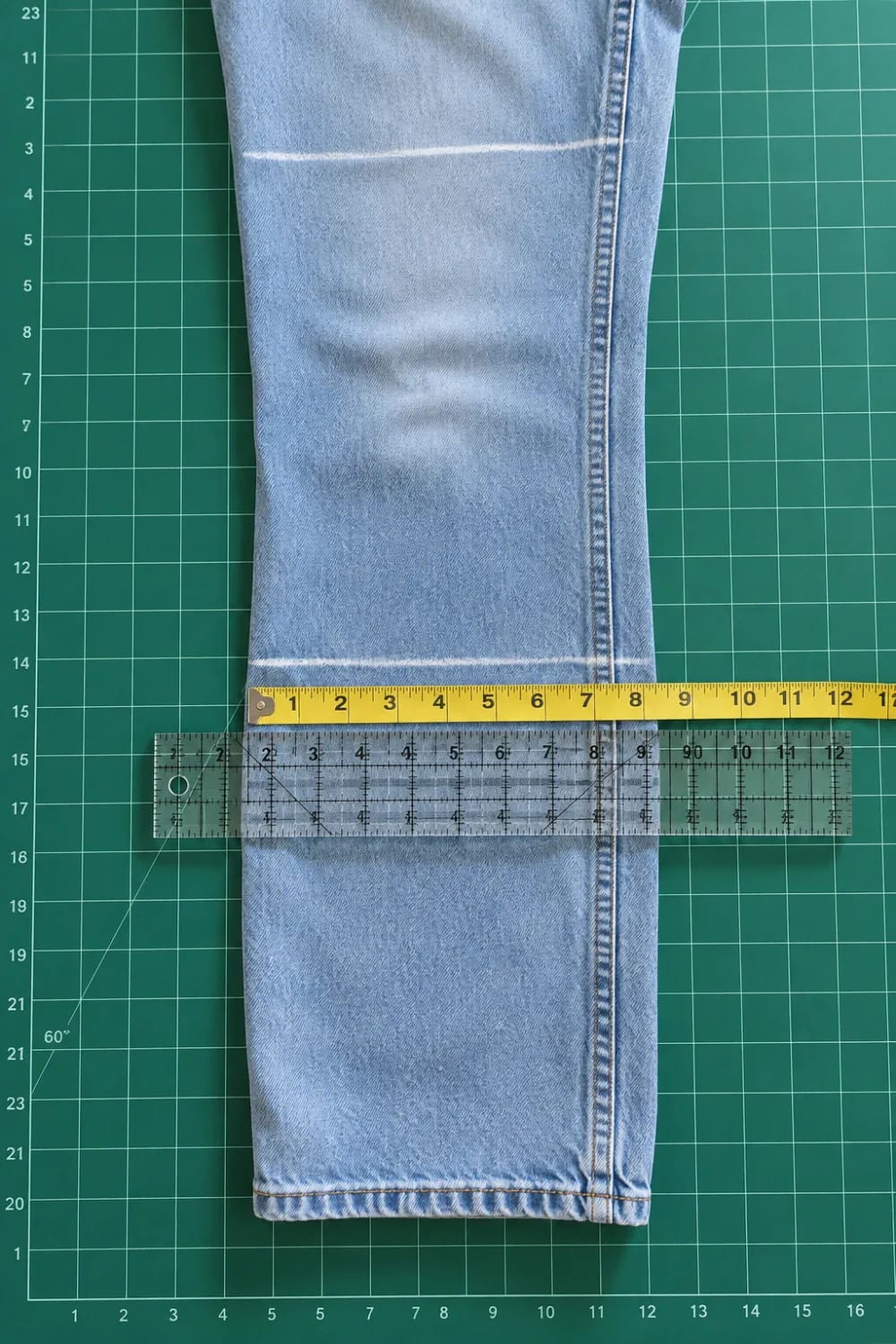Denim Bucket Bag Jean Leg Measurement A denim jean leg lies on a green gridded cutting mat with a yellow tape measure and clear quilting ruler marking its width for a denim bucket bag project