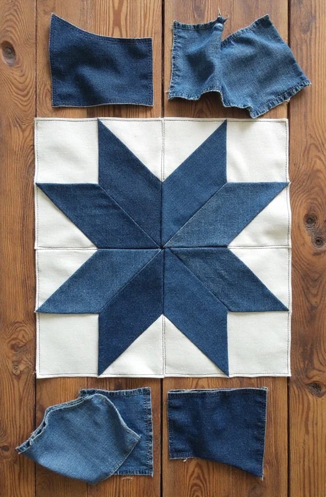 Denim Fabric Star Ornament From Old Jeans Pieced sawtooth star made from four washes of blue denim on white fabric, surrounded by cut pieces of old jeans on a wooden surface