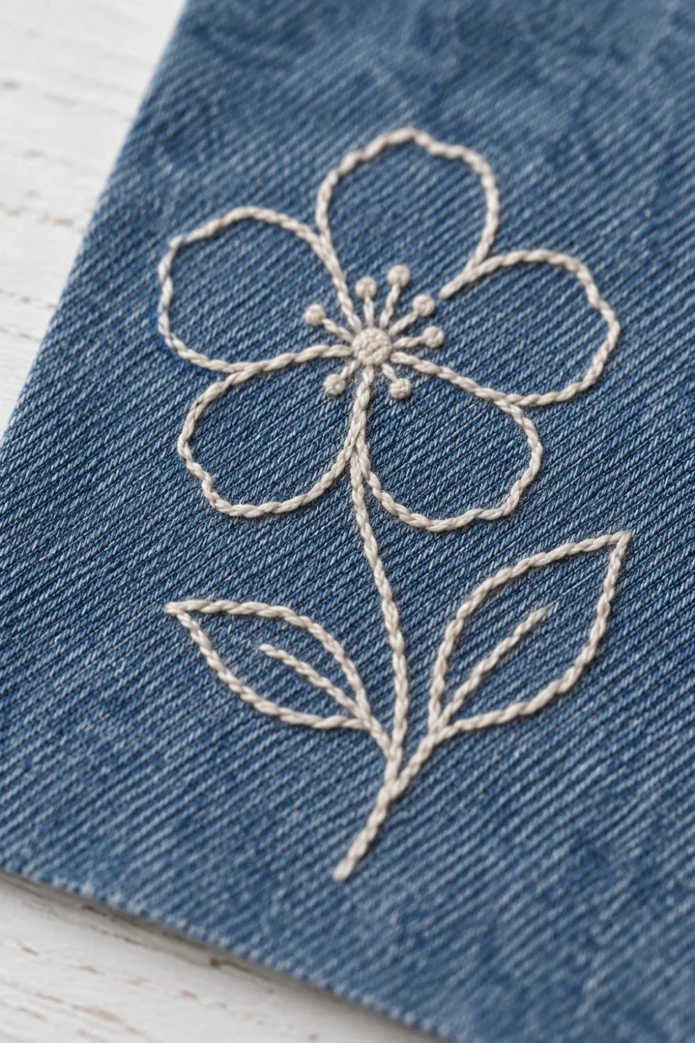 Floral Embroidered Hem Jeans Detail Close-up of blue denim showing cream embroidered flowers and leaves near the hem, illustrating floral embroidered hem jeans.