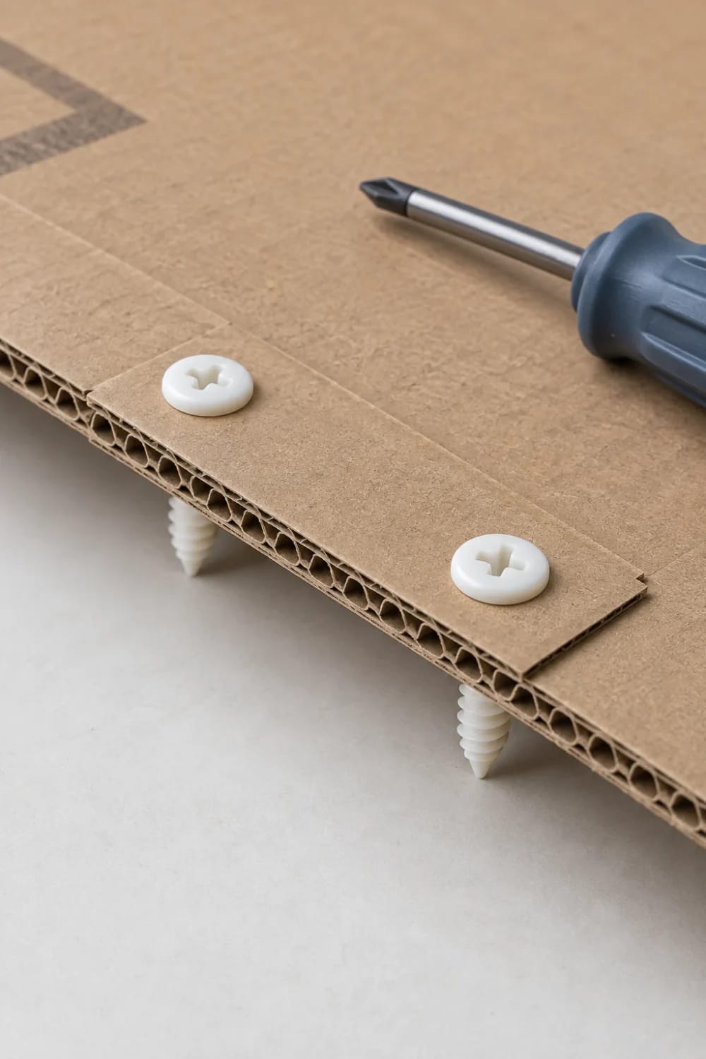 Close-up of corrugated cardboard panels joined with white fasteners, a screwdriver, and plastic supports for a cardboard castle playhouse project