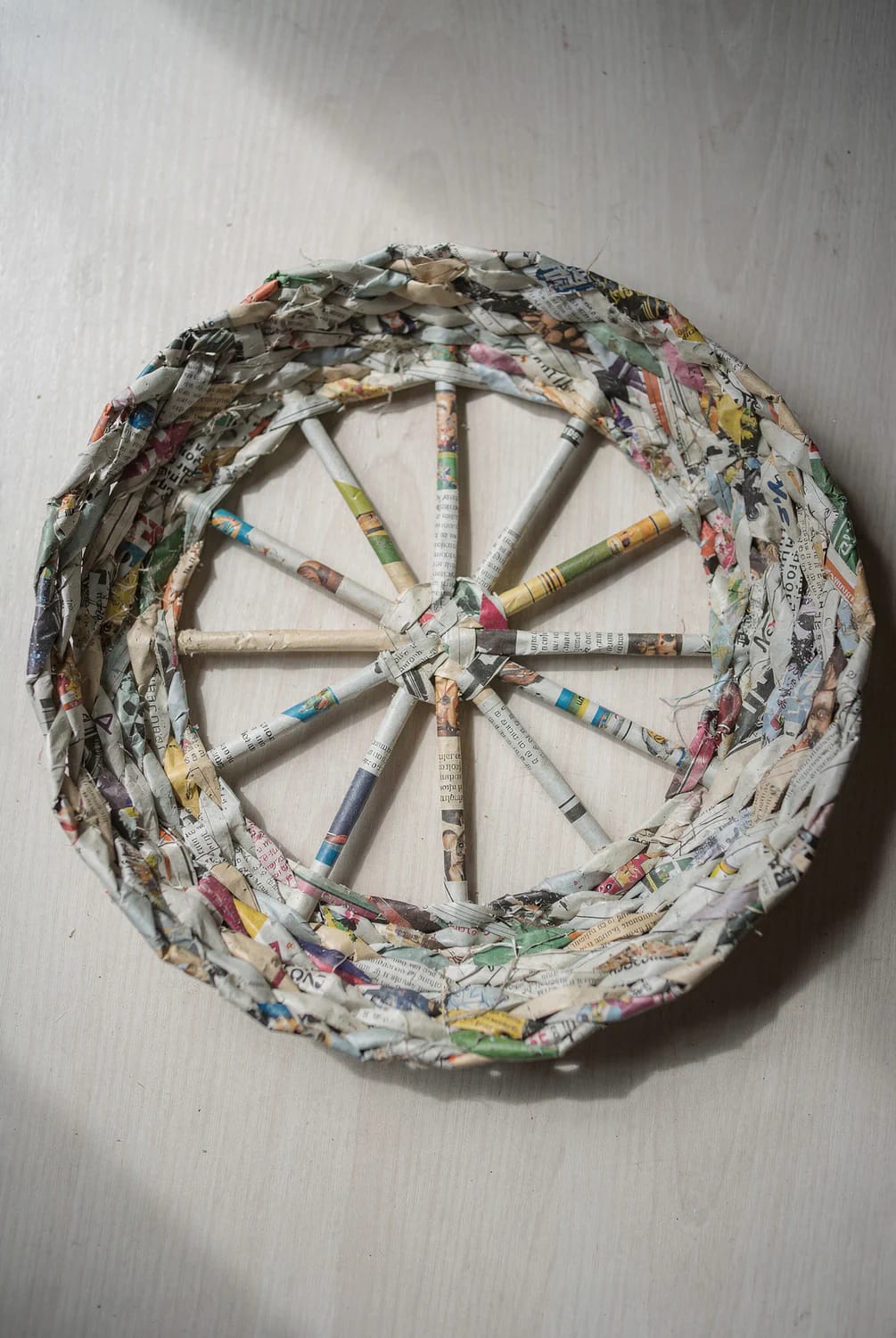 Round newspaper basket base made from rolled paper tubes, with an odd number of spokes radiating from the center and woven newspaper sides around the edge