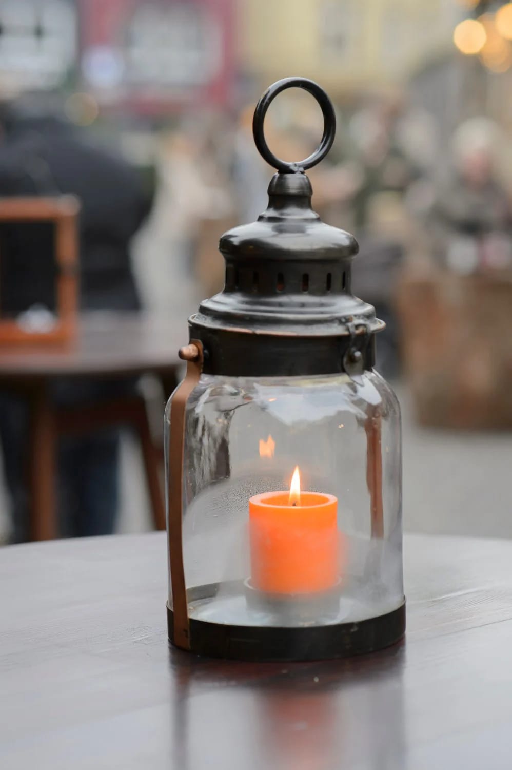 A black metal and glass lantern holding a lit orange candle sits on a living room centre table, illustrating an out of waste showpiece that throws light