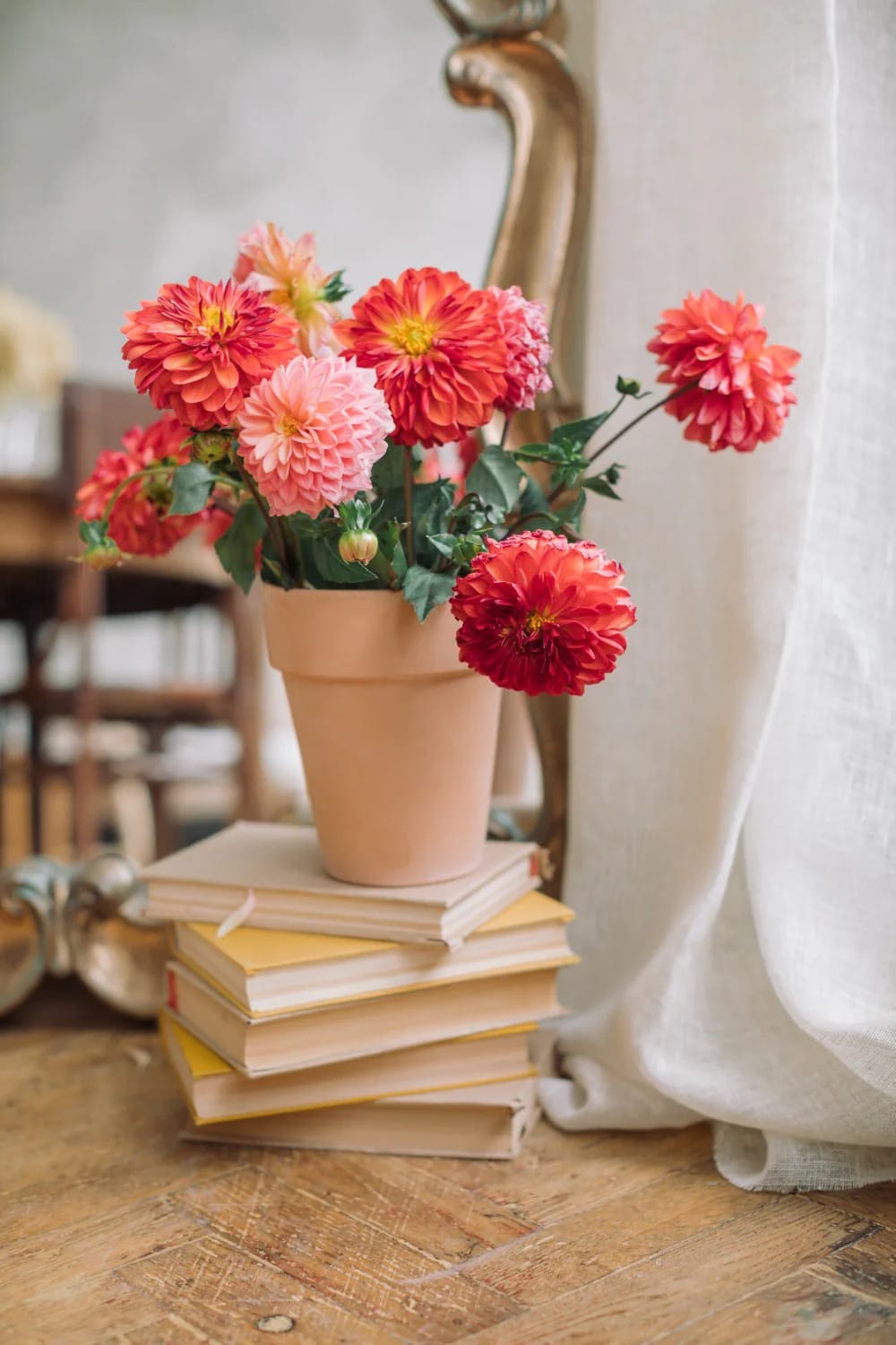 Terracotta flower pot filled with coral and pink flowers resting on a stack of books on a wooden table, illustrating an out of waste living room centre table showpiece