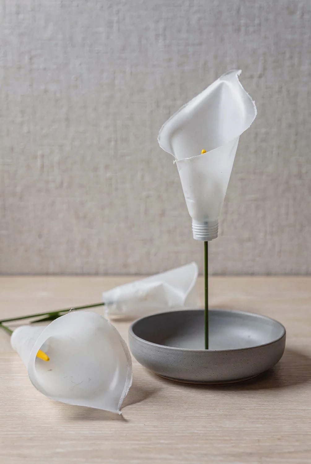 Shaping Plastic Bottle Flower Chandelier Blooms White plastic bottle pieces shaped into flower blooms on green stems, with loose flower parts beside a gray bowl during the shaping process for a party ceiling chandelier