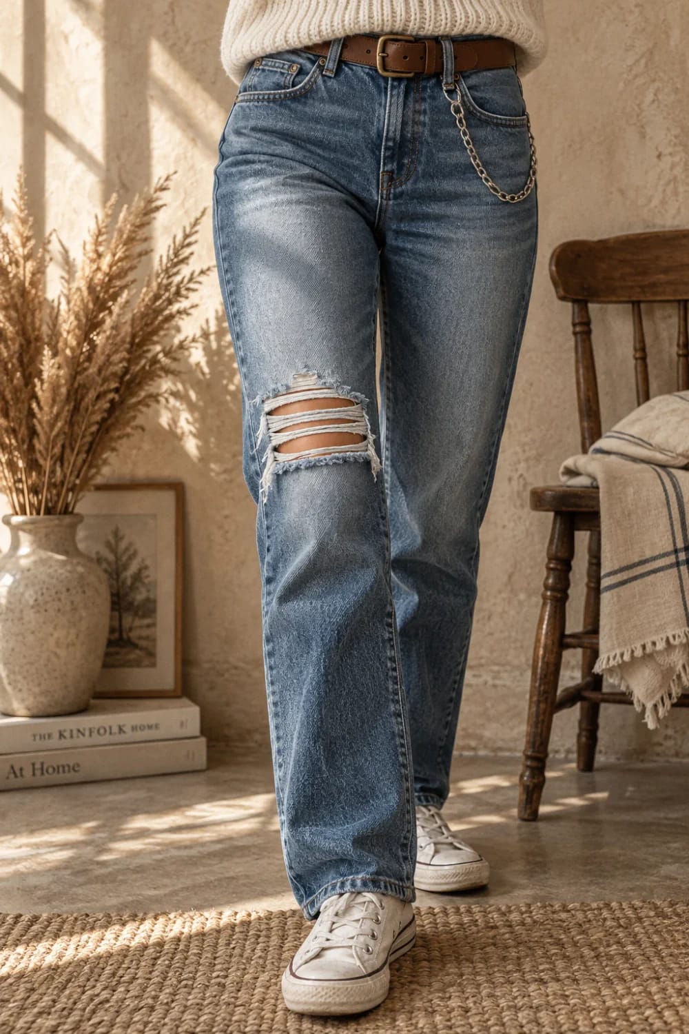 Person wearing blue jeans with horizontal ladder-style slashes positioned above the kneecap, paired with white sneakers and a brown belt