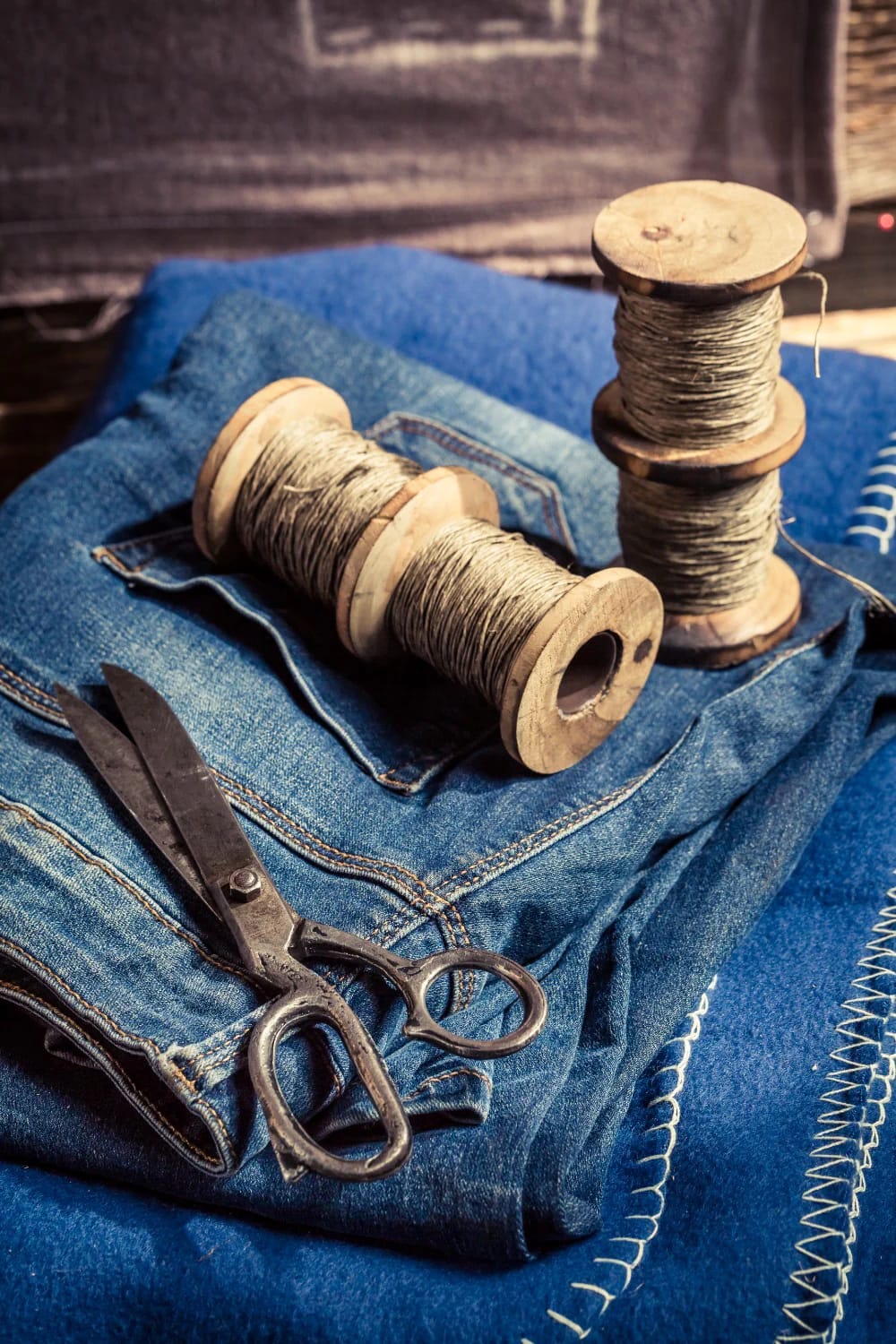 Thread and Denim Wooden thread spools and metal scissors on folded blue denim fabric